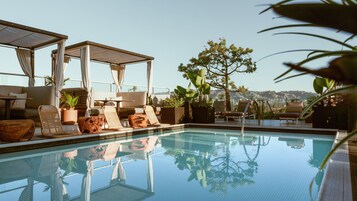 Un área de piscina en la azotea con sillones de descanso, una pérgola y plantas en macetas.