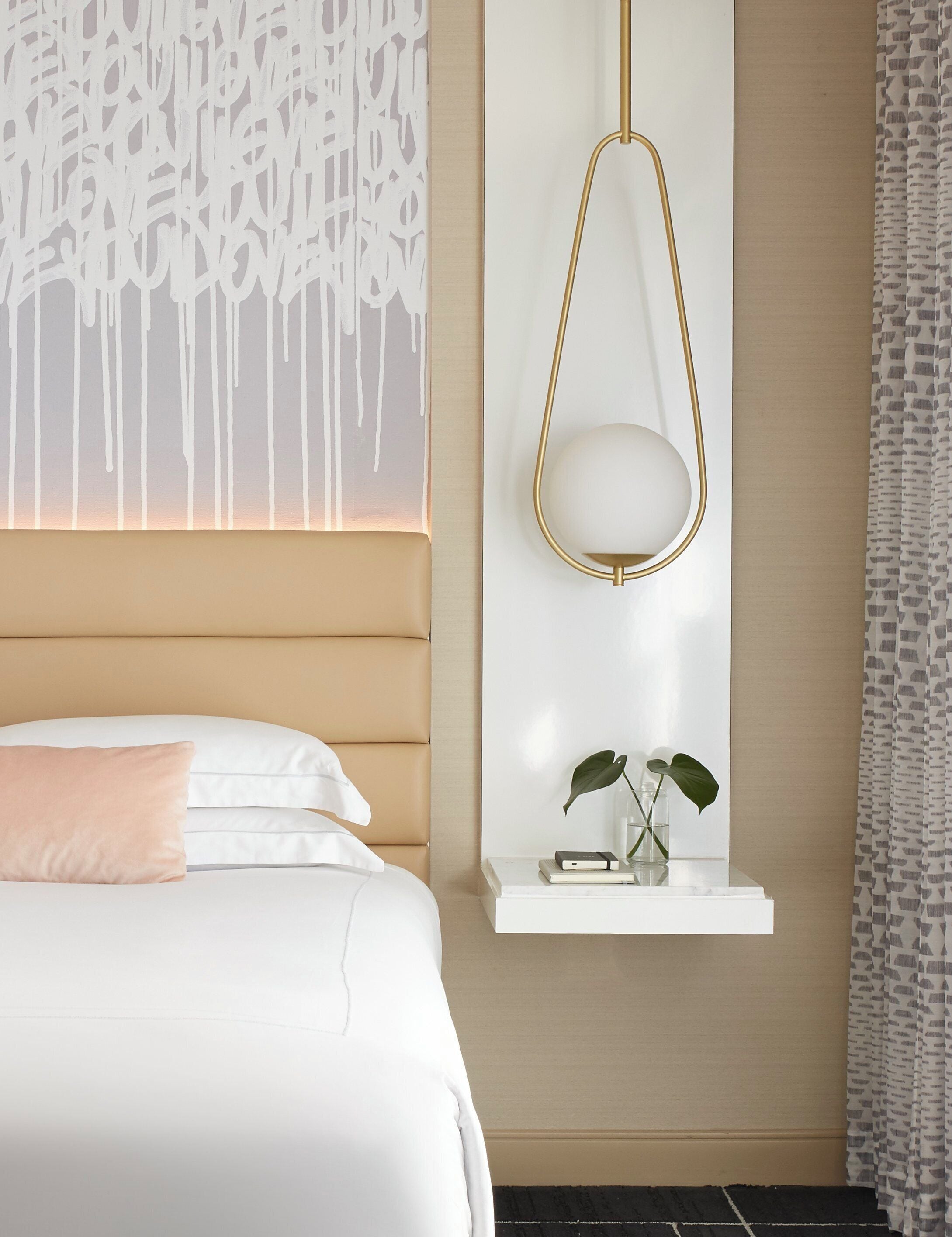 A hotel room with a bed, a bedside table with a lamp, and a wall with a decorative pattern.