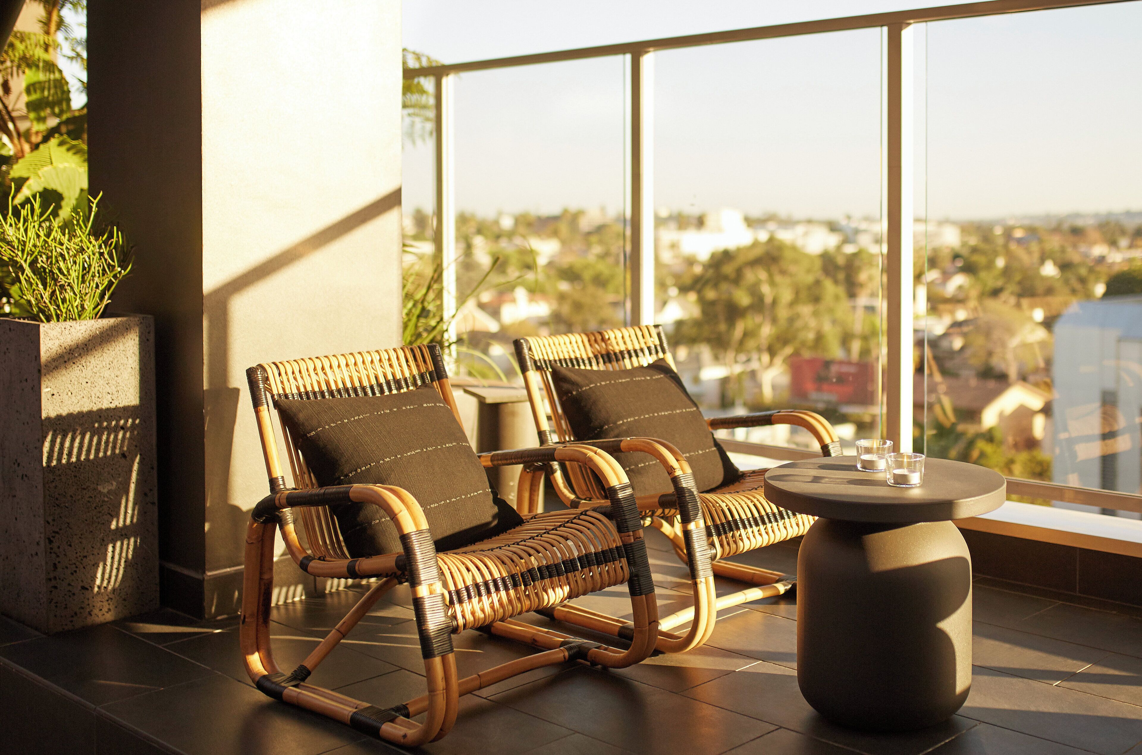 A balcony with wicker chairs and a table, overlooking a cityscape.