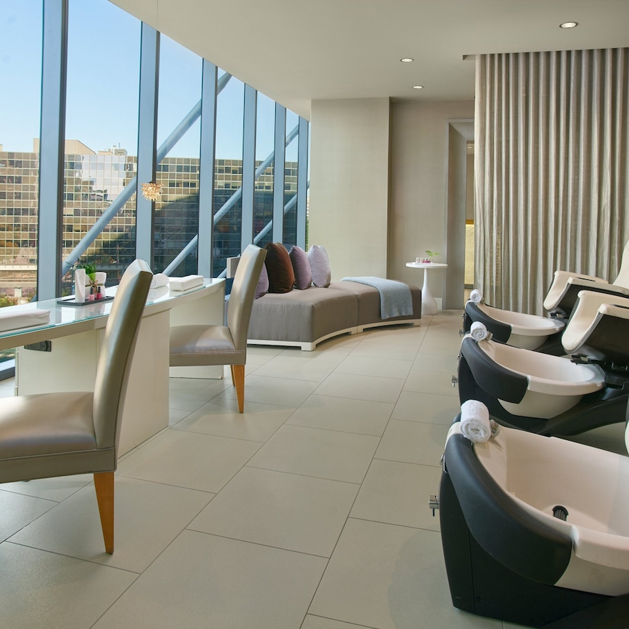 A modern hotel room with a large window offering a city view, a comfortable seating area with a sofa and chairs, and a small table with a vase.
