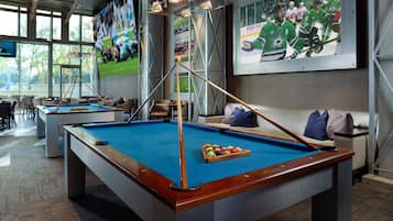 A pool table with a billiard cue, a sofa, and a large sports poster on the wall.