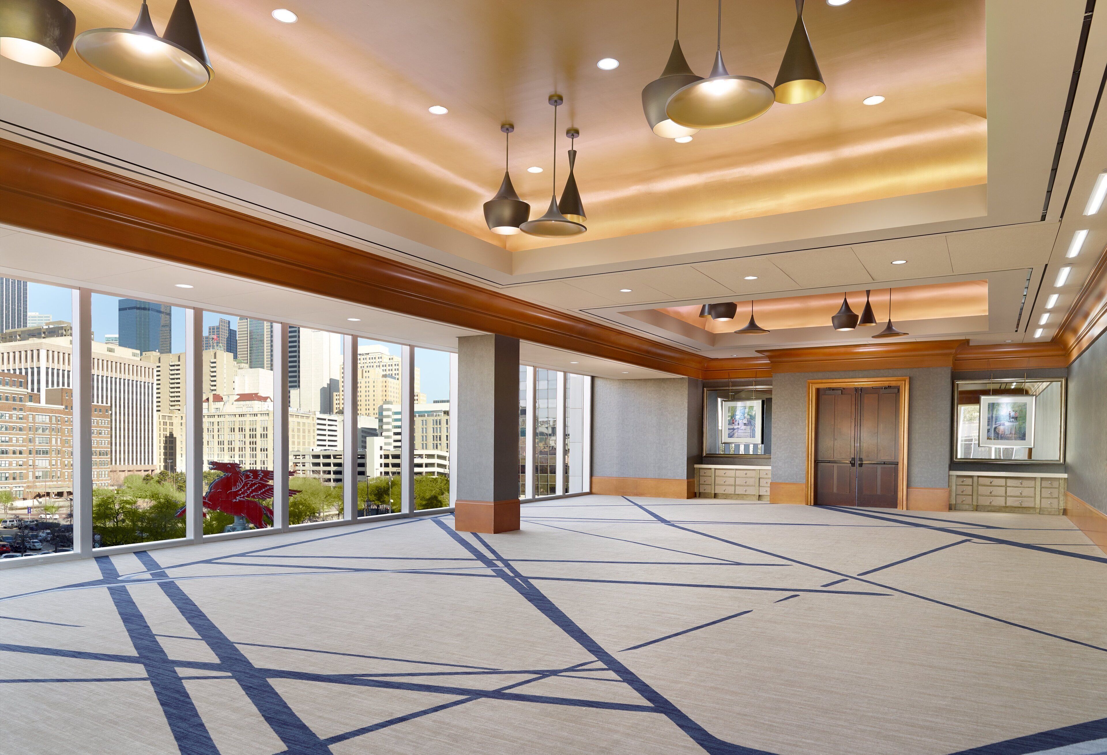 A spacious hotel lobby with large windows, modern pendant lighting, and a view of the cityscape.