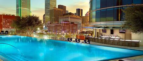 A swimming pool with lounge chairs, a bar area, and a cityscape view in the background.