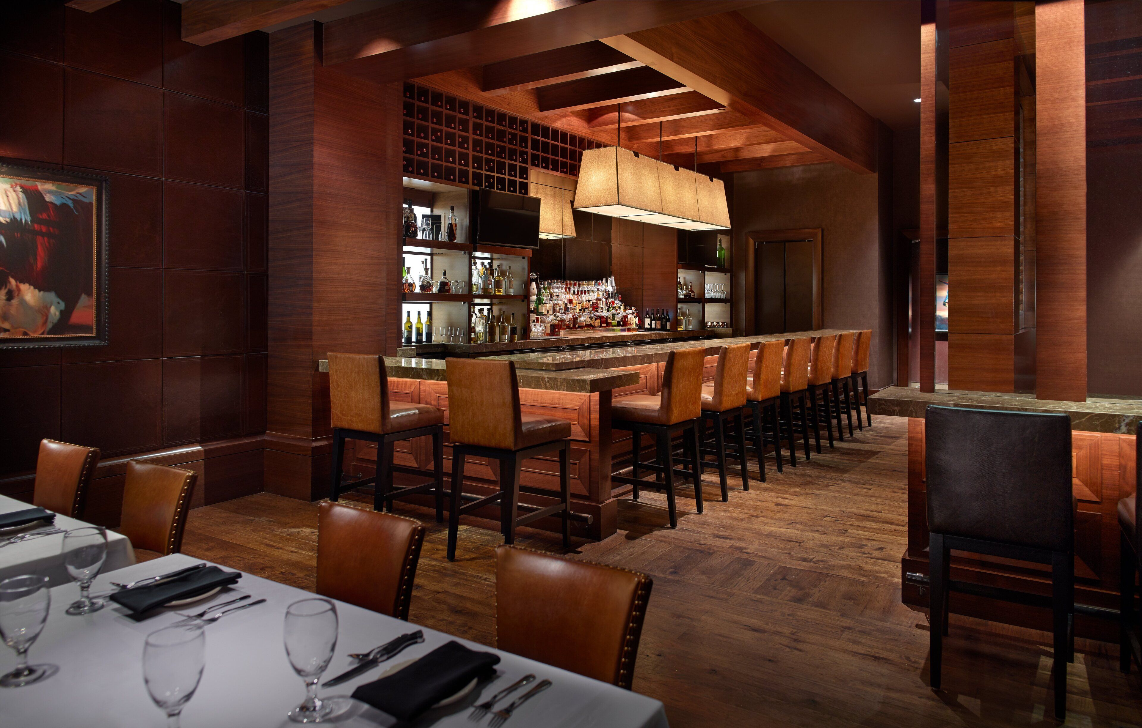 A restaurant with a long bar, wooden chairs, and a high ceiling.