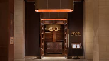 Un vestíbulo con diseño moderno, que presenta un amplio mostrador de recepción de madera, una lámpara colgante y un cartel de Bob's Steak & Chop House.