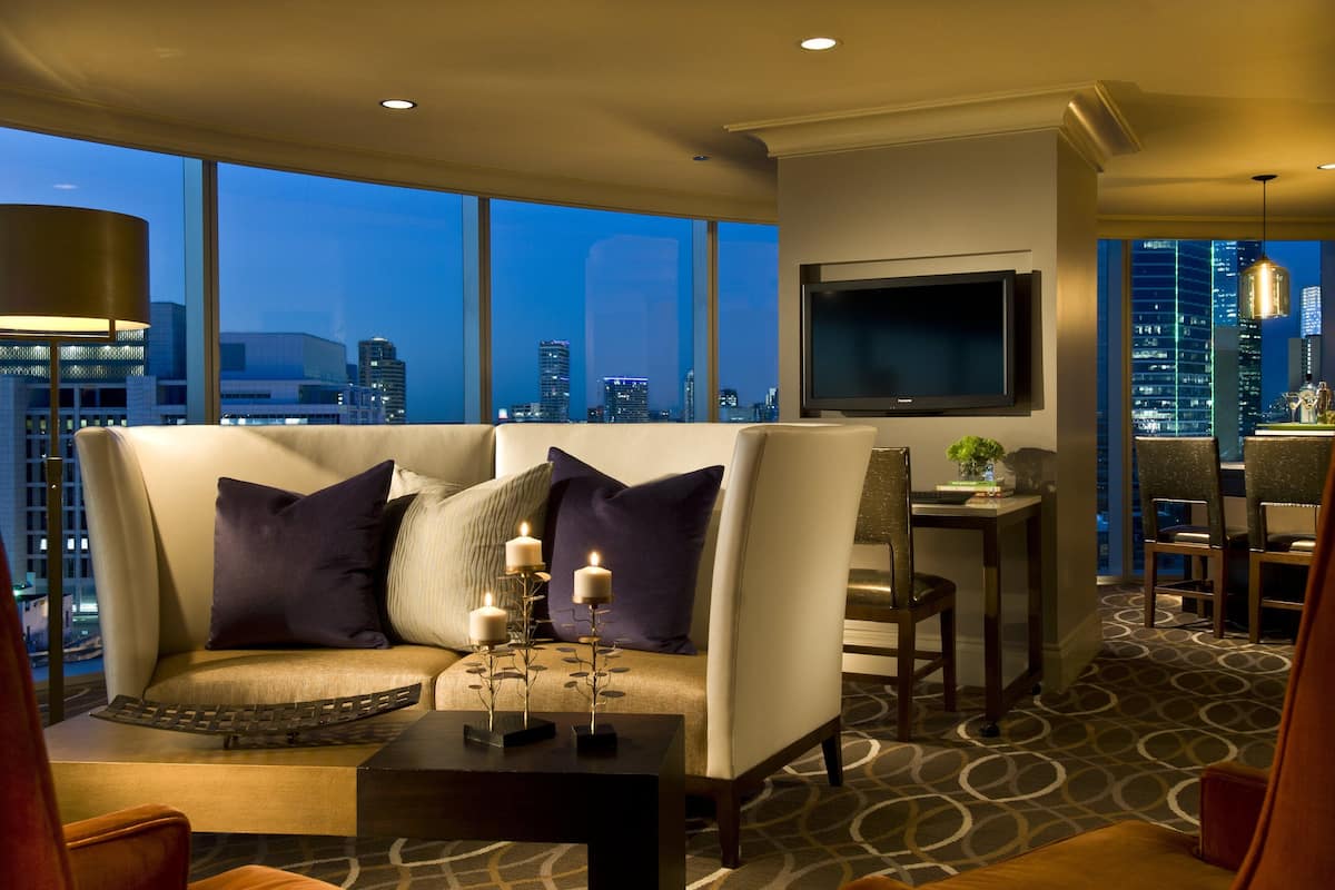 Ein modernes Hotelzimmer mit großem Fenster und Blick auf die Stadt, einer Couch mit Dekokissen, einem kleinen Tisch mit Kerzen und einem an der Wand befestigten Flachbildfernseher.