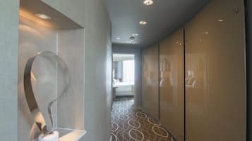 A modern hotel corridor with a unique metal sculpture, a patterned carpet, and a glimpse of a room with a bed and a window.