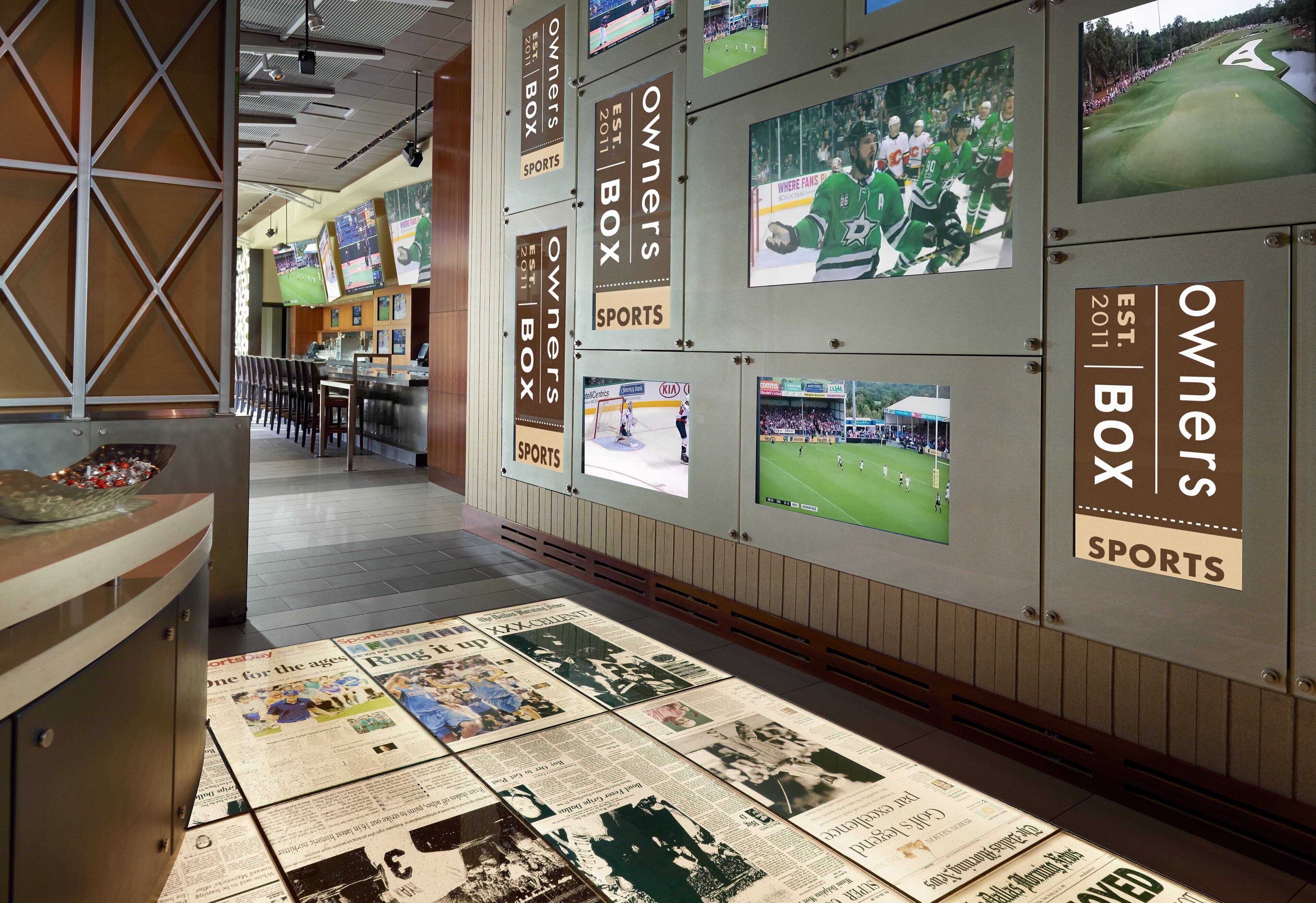 Corredor com tema esportivo, decorado com itens de coleção esportiva emoldurados e chão coberto com jornais.