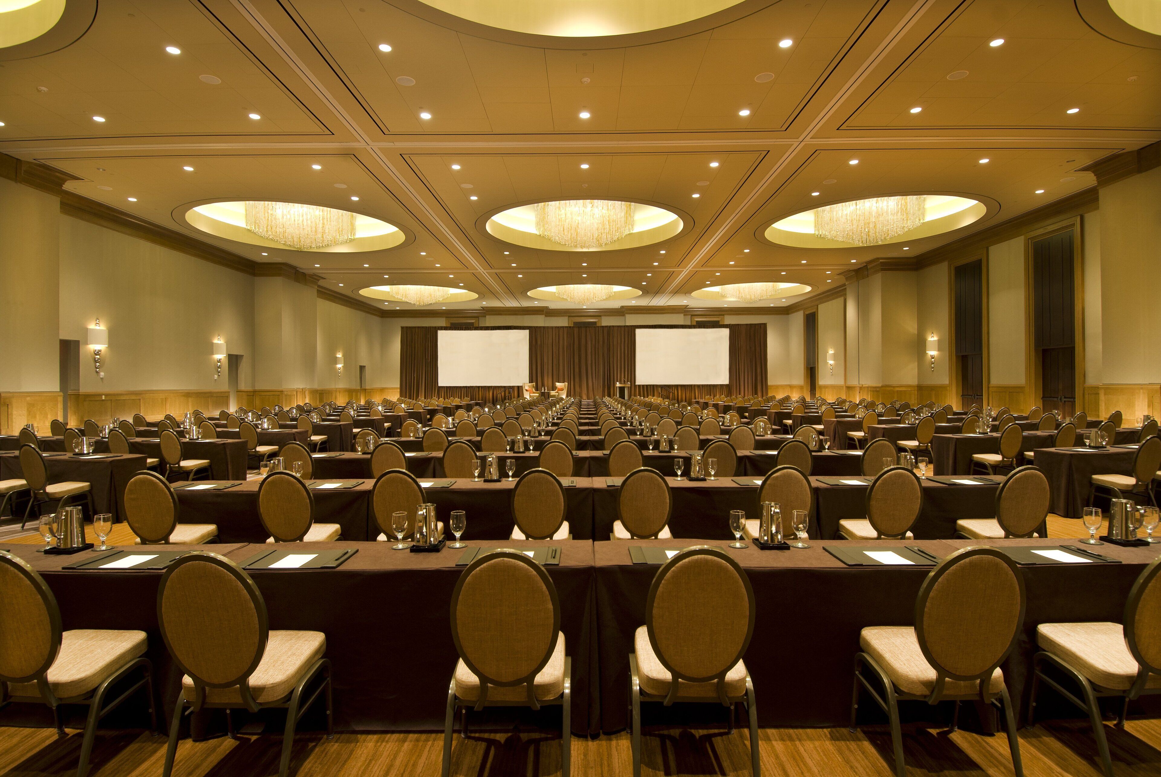 A large conference room with rows of tables and chairs, equipped with projectors and screens.
