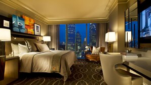 A hotel room with a large bed, a desk, a chair, and a view of the city skyline at night. - Omni Dallas Hotel (Dallas)