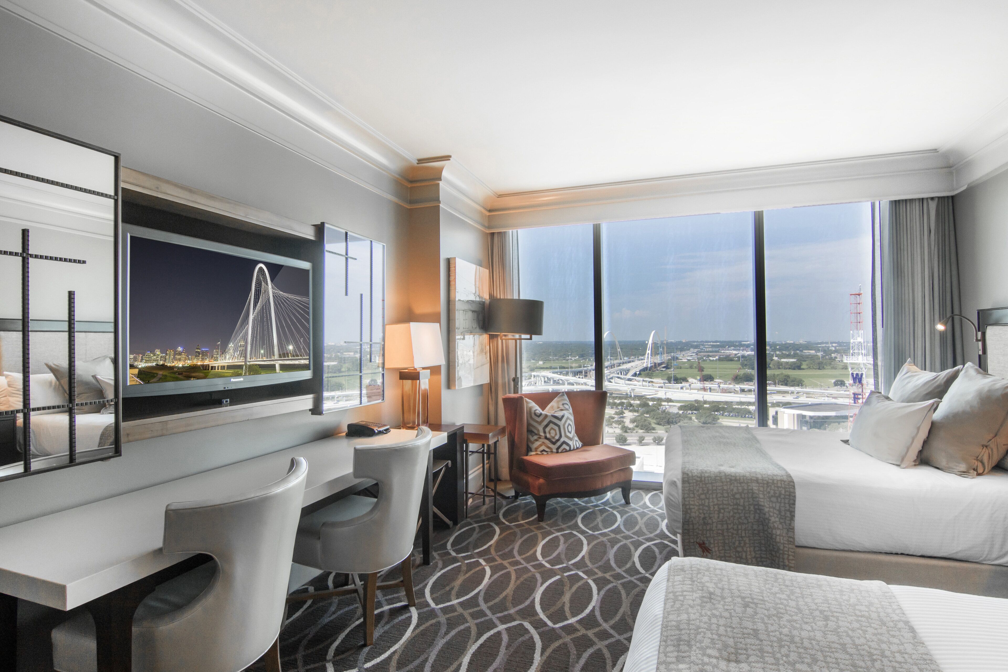 A hotel room with a large window, a bed, a desk, a chair, and a sofa.