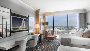 A hotel room with a large window, a bed, a desk, a chair, and a sofa.