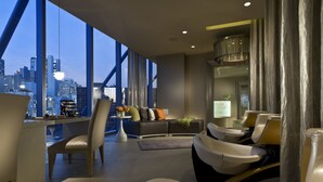 A modern hotel room with a city view, a sofa, a massage chair, and a small table with a vase of flowers. - Omni Dallas Hotel (Dallas)