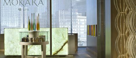 A reception area with a marble counter, a glass display table with bottles, and a decorative wall with a wavy pattern.