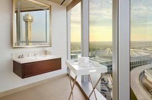 A modern bathroom with a large mirror, a white vanity, and a view of a cityscape through large windows.