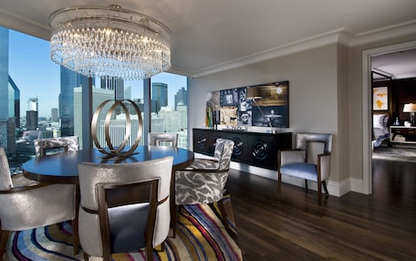 A modern living room with a city view, a chandelier, a dining area with chairs, a sofa, a TV, and a cabinet.