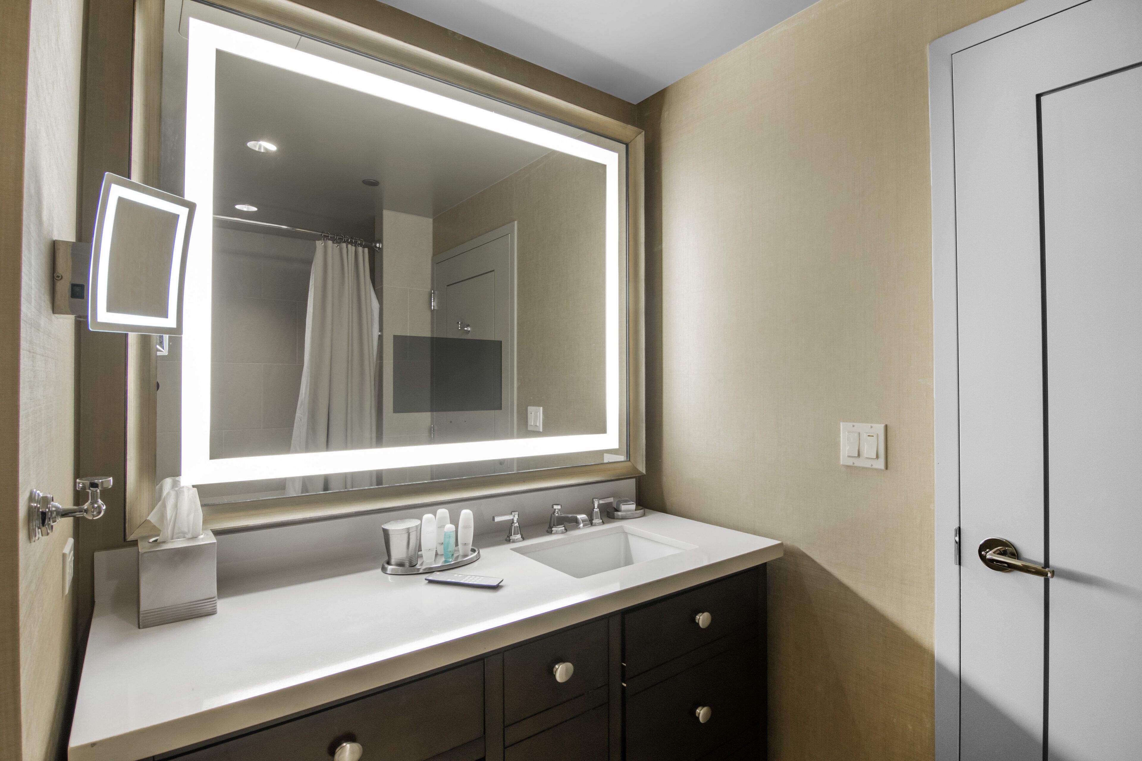 A bathroom with a large mirror, two sinks, a towel rack, and a door.