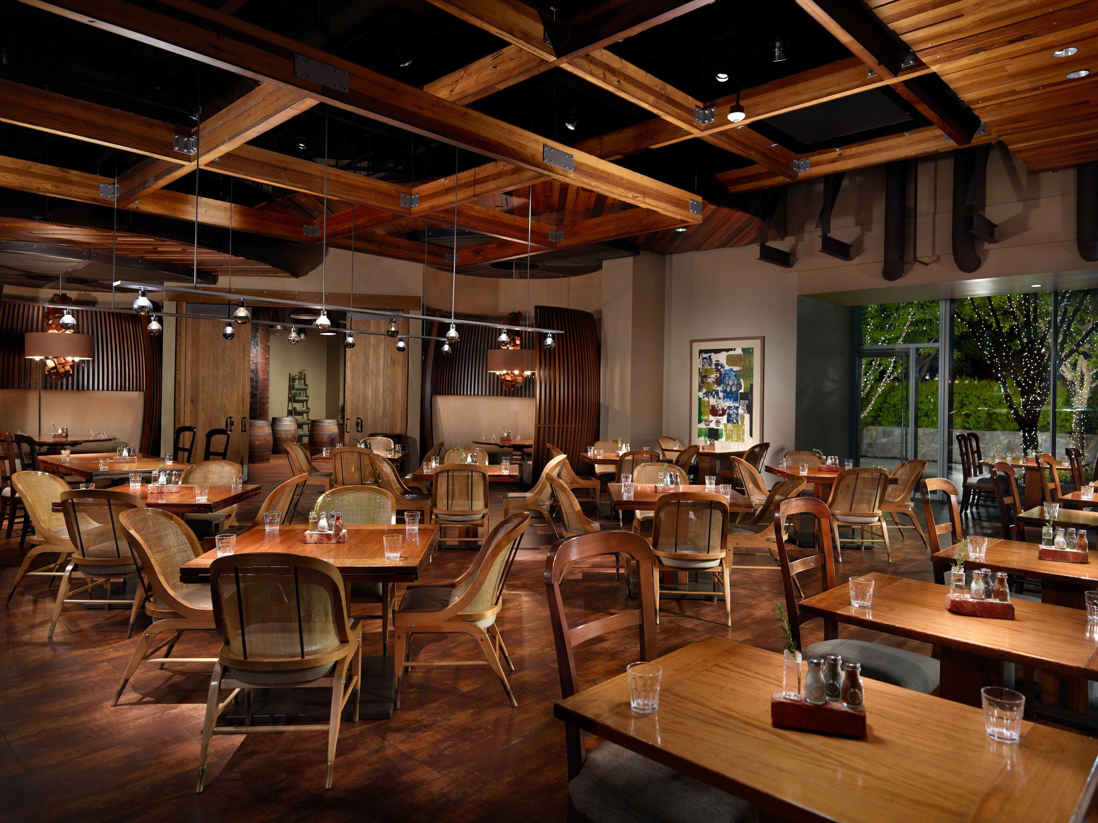 A spacious restaurant with wooden tables and chairs, exposed ceiling beams, and pendant lighting.