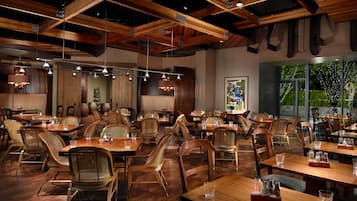 A spacious restaurant with wooden tables and chairs, exposed ceiling beams, and pendant lighting.