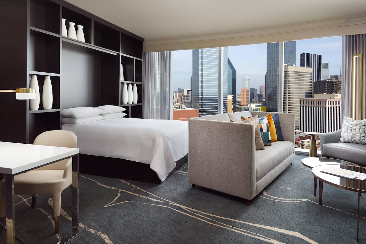Ein modernes Hotelzimmer mit Bett, Sofa und Essbereich, mit Blick auf die Stadtlandschaft.
