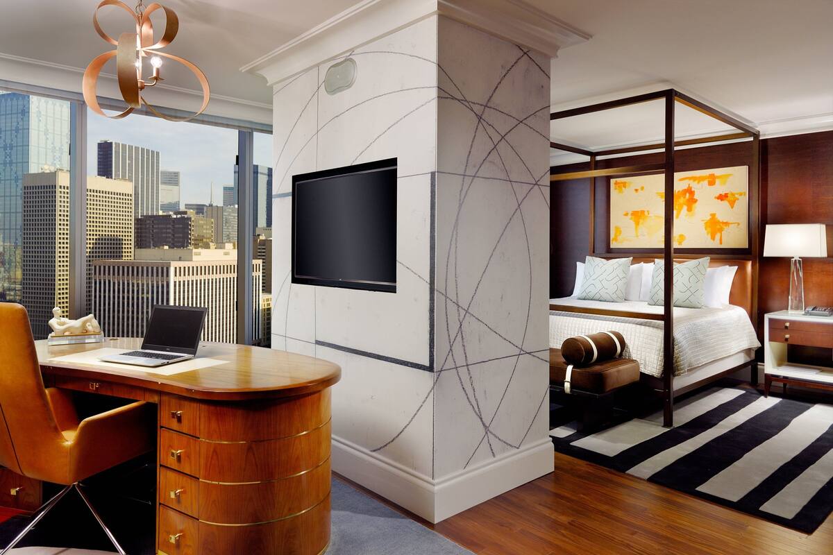Ein modernes Hotelzimmer mit Stadtblick, ein Schreibtisch mit Laptop, ein Bett mit Aussicht und ein großes Kunstwerk an der Wand.