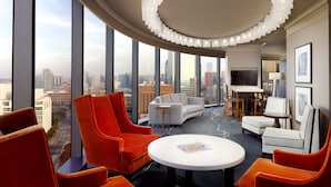 A modern hotel room with a curved ceiling, large windows offering a city view, a round table, and orange and white furniture. - Omni Dallas Hotel (Dallas)