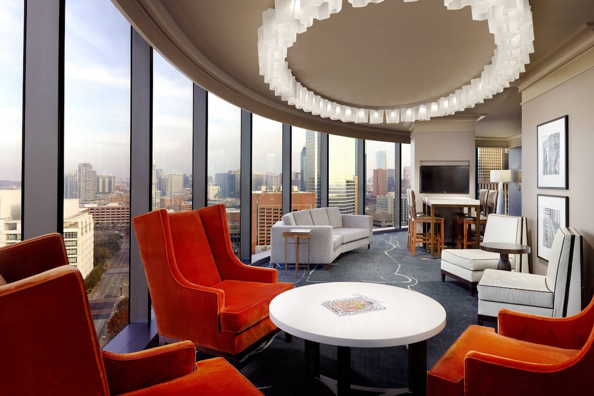 Ein modernes Hotelzimmer mit gewölbter Decke, großen Fenstern mit Blick auf die Stadt, einem runden Tisch und orange-weißen Möbeln.