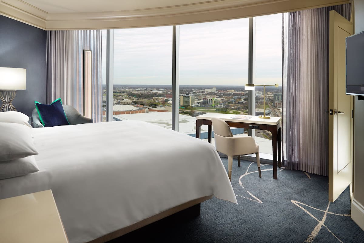 Ein Hotelzimmer mit einem großen Bett, einem Schreibtisch und Blick auf die Stadt.