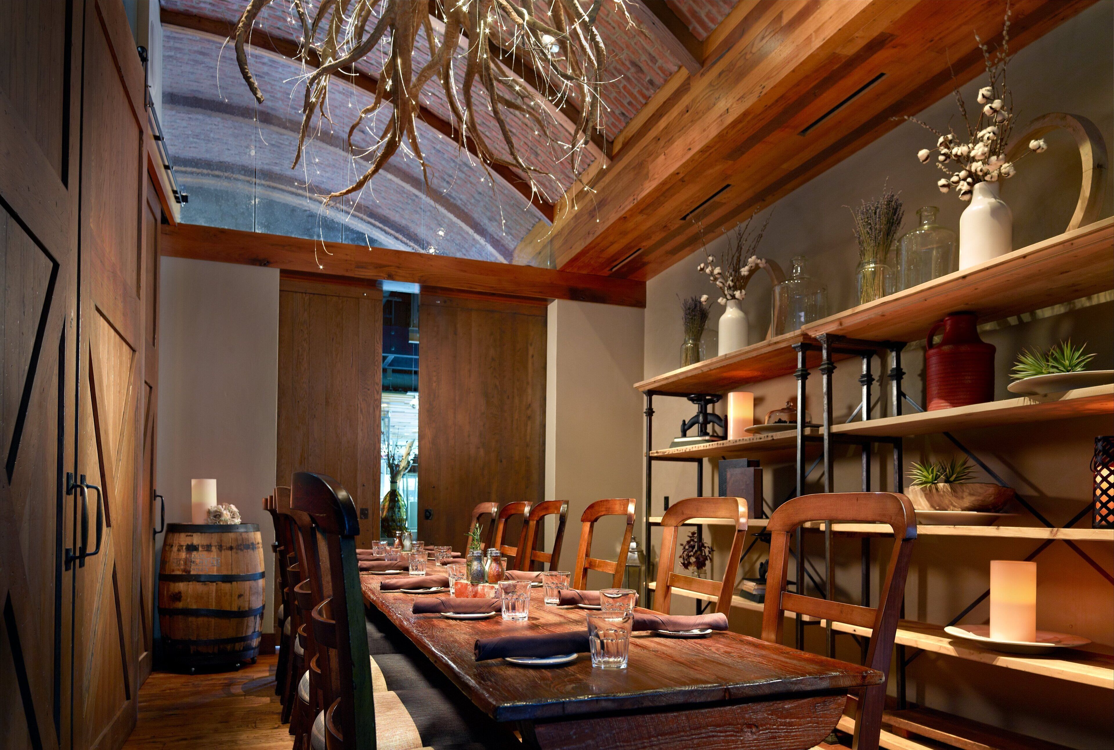 Une longue table à manger en bois, accompagnée de chaises, d’un tonneau et d’étagères ornées d’objets décoratifs.
