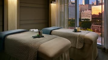 A hotel room with two massage tables, a city view, and a large window.