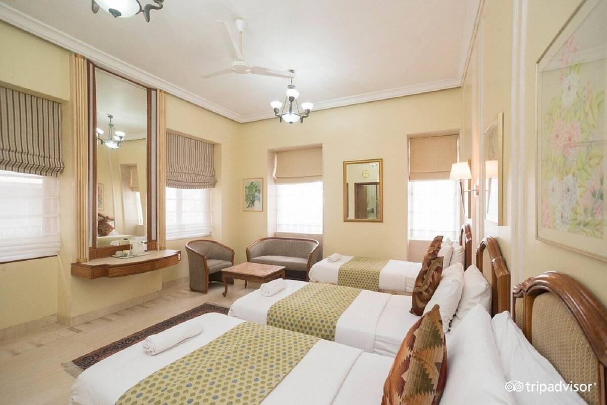 A hotel room with two single beds, a sofa, a chair, a desk, and a large mirror.