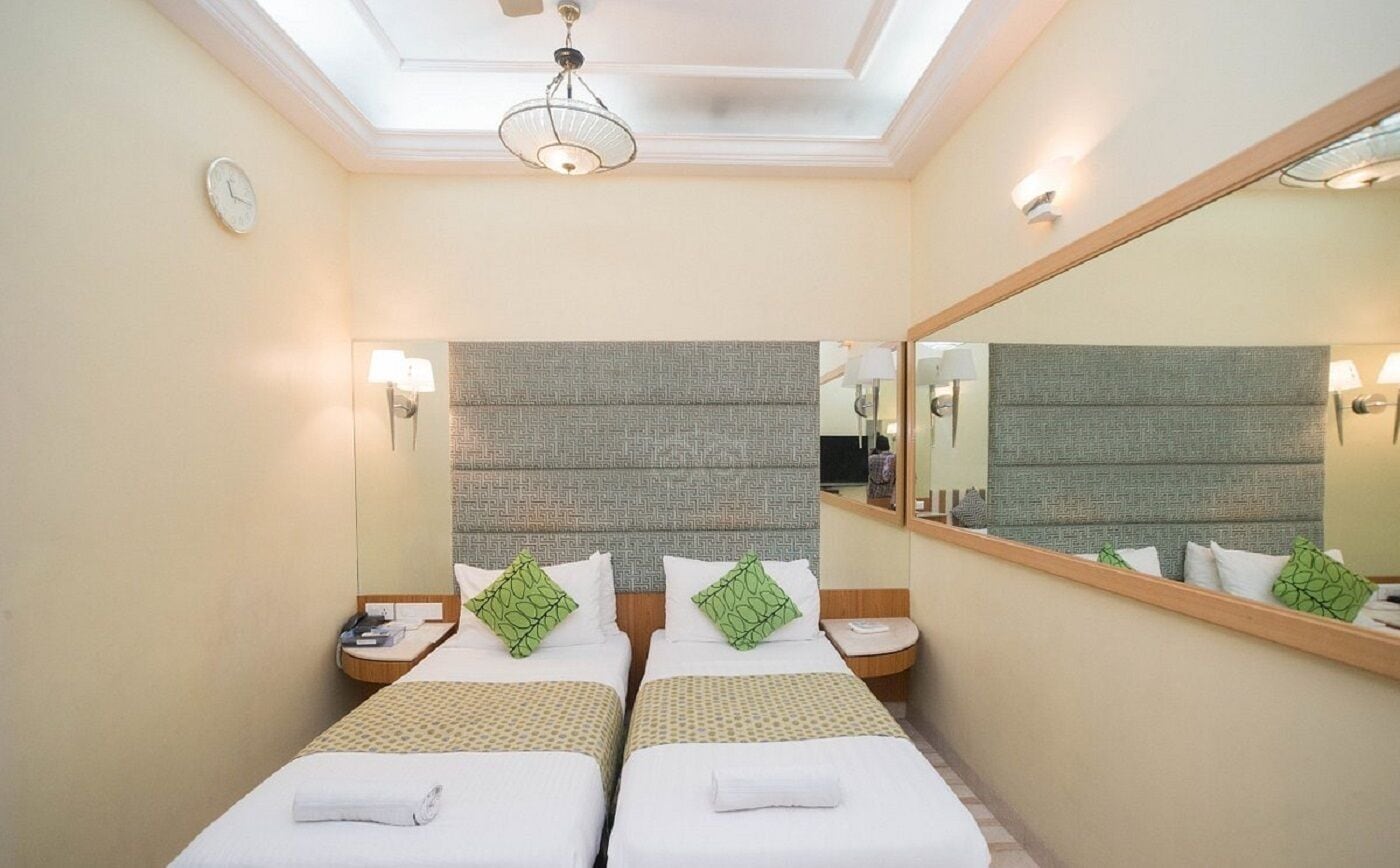 A hotel room with two beds, a large mirror, and a ceiling light.