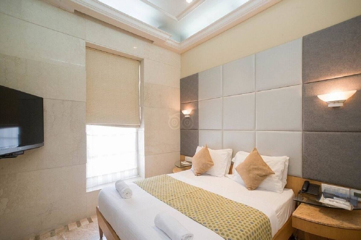 A hotel room with a large bed, a flat-screen TV mounted on the wall, and a window with a blind.
