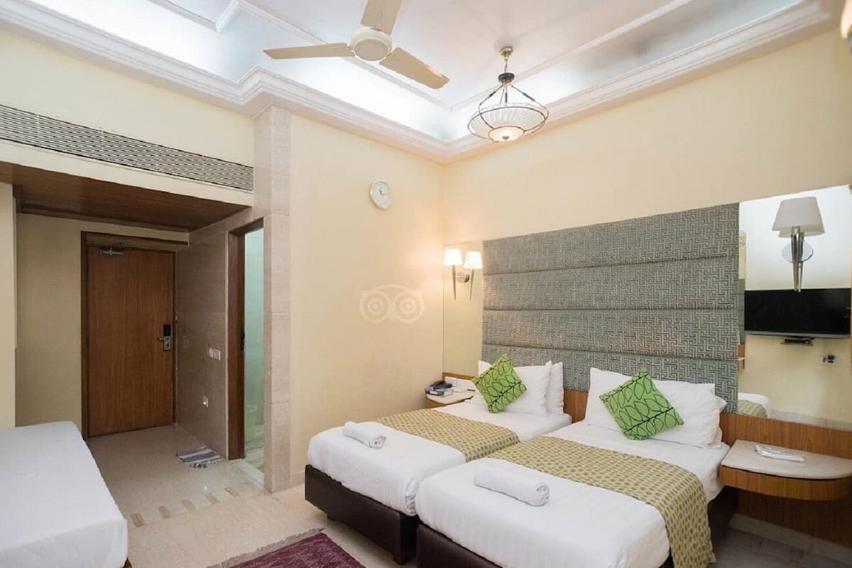 A hotel room with two beds, a ceiling fan, a bedside table with a lamp, and a television.