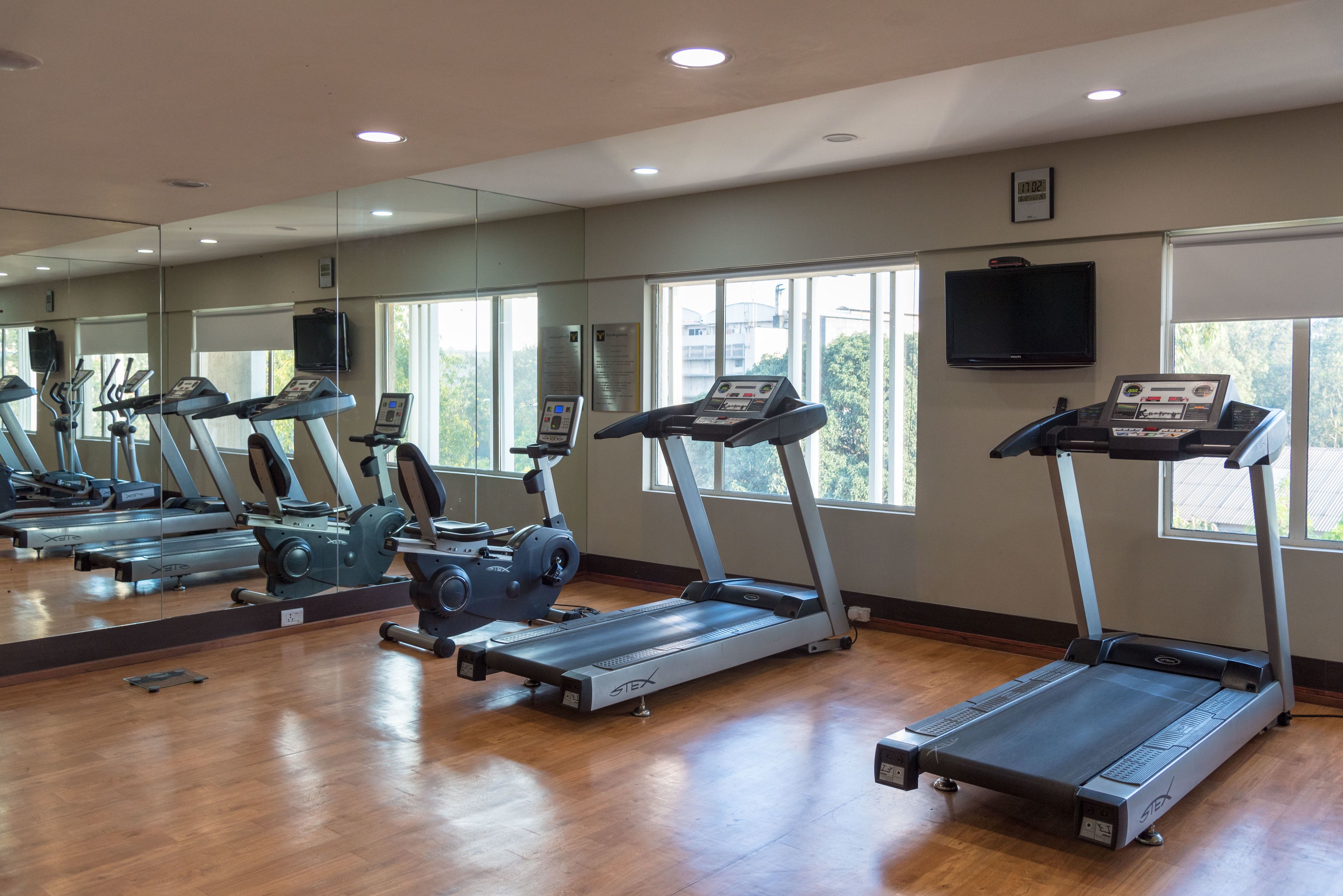 A gym with multiple treadmills, a large mirror, and windows with natural light.