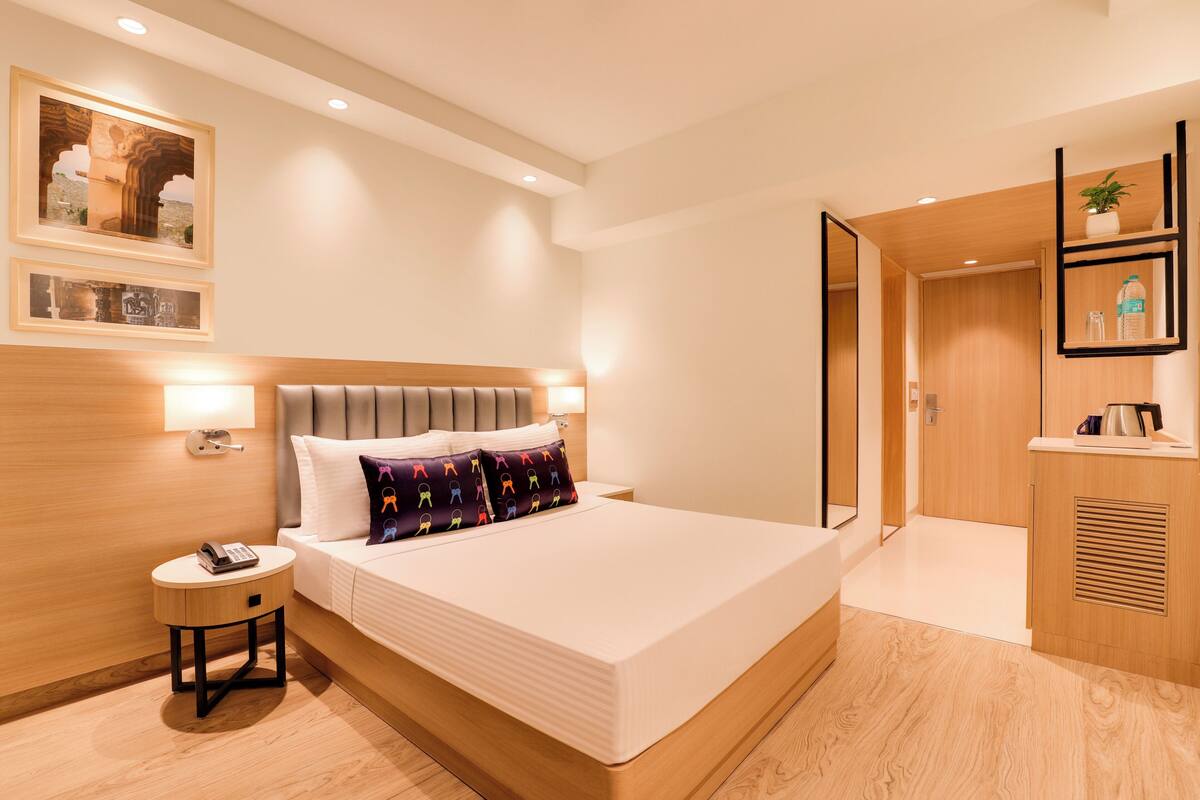 Quarto de hotel moderno com cama grande, mesa de cabeceira e uma pequena mesa redonda com um telefone.