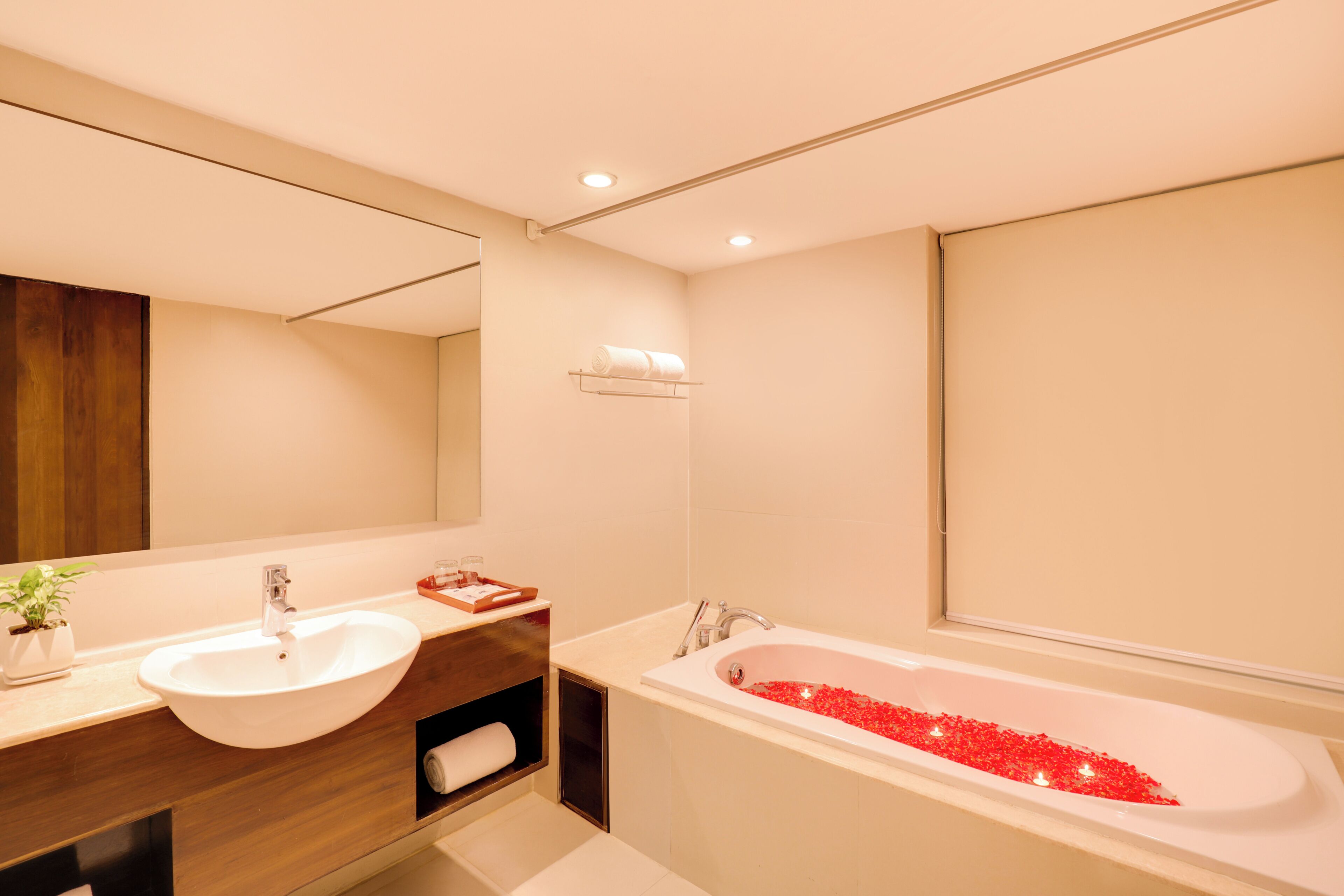 A bathroom with a sink, mirror, and bathtub filled with red pebbles.