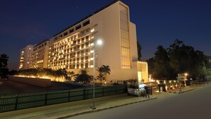 Un hôtel à plusieurs étages, doté de fenêtres illuminées, d’une entrée sécurisée par un portail et d’un espace paysager agrémenté d’arbres.