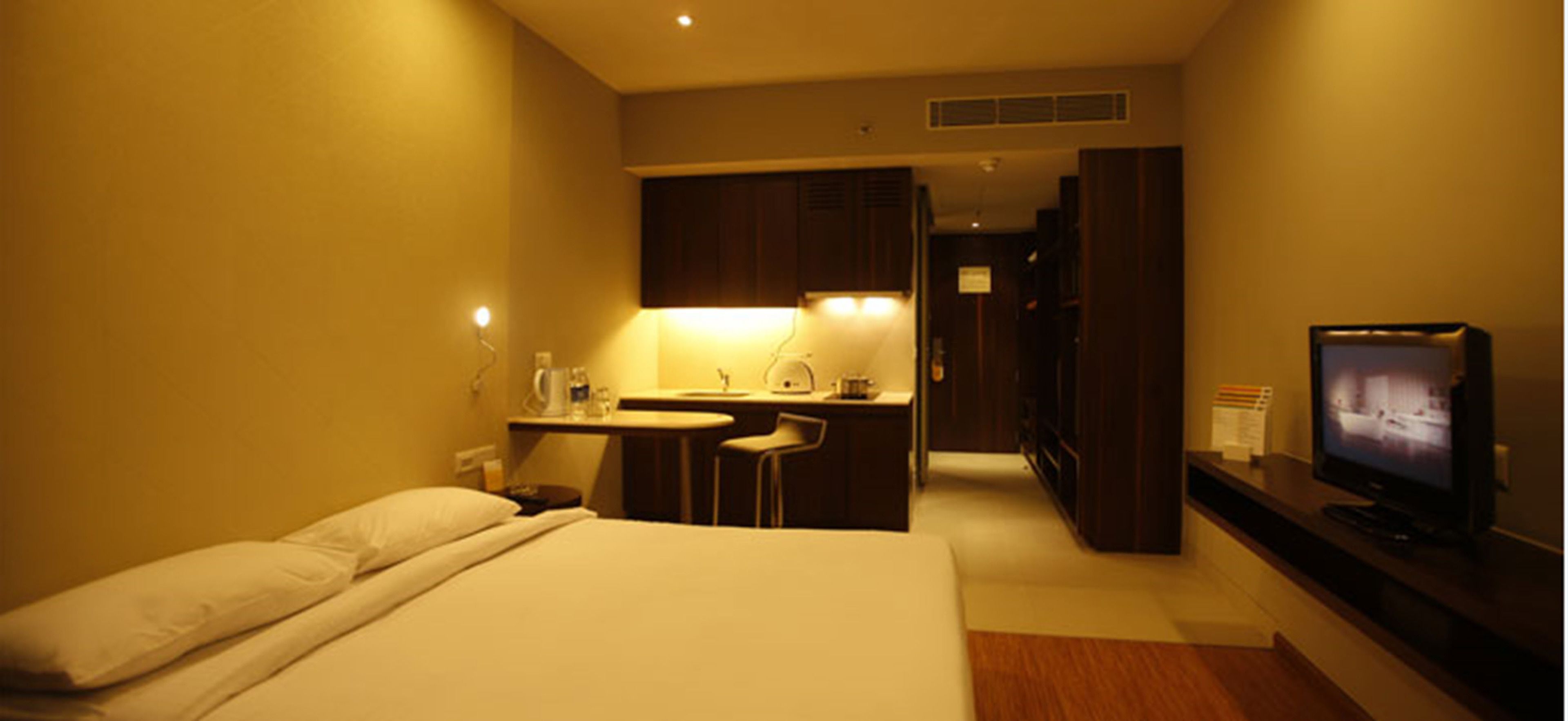 Una habitación de hotel con cama, escritorio, silla, televisor y kitchenette.
