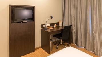 Una habitación de hotel con un escritorio de madera, una silla de oficina negra, un televisor, una lámpara y una cama.