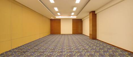A large, empty room with a patterned carpet, recessed ceiling lights, and plain walls.