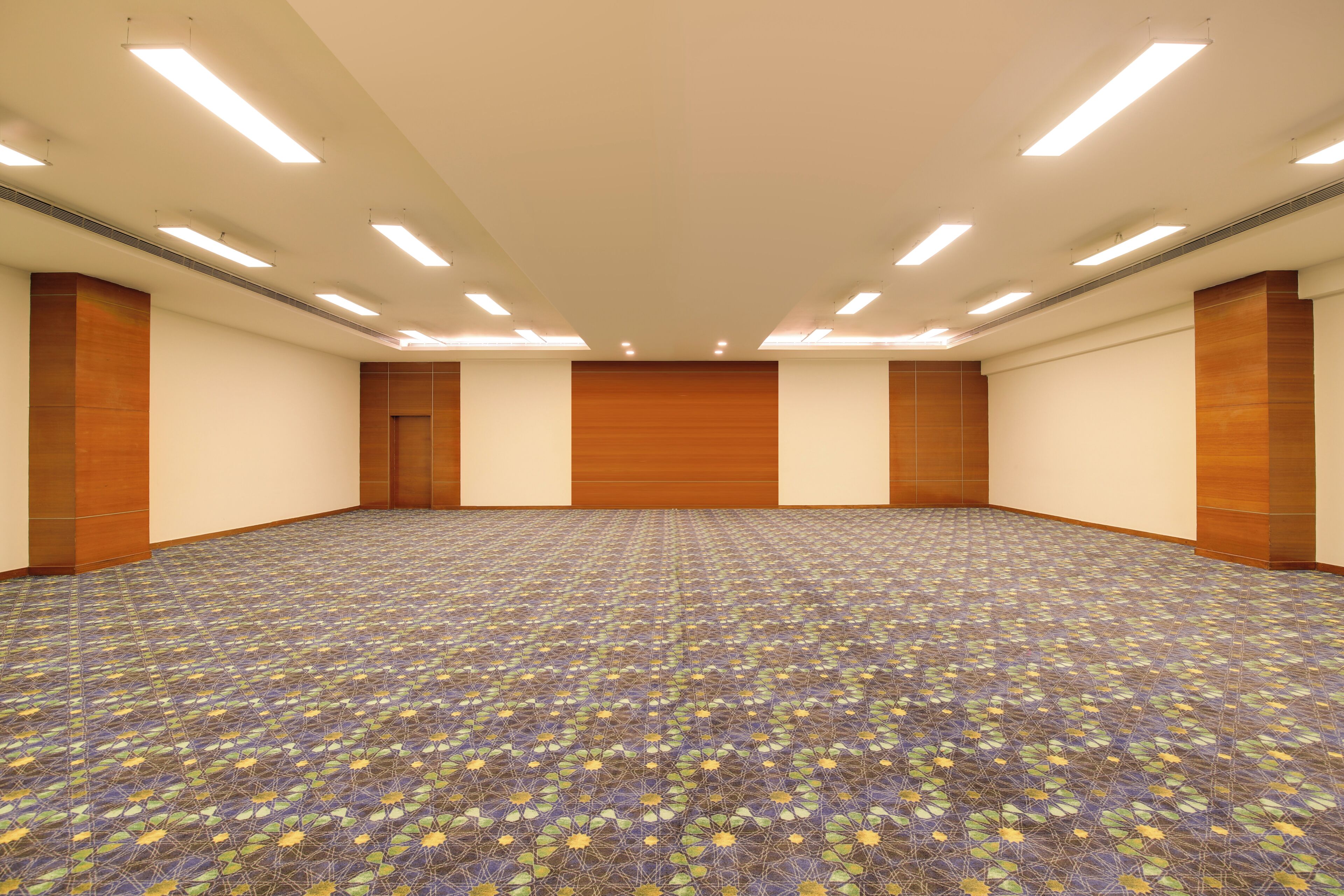 Un amplio salón de conferencias con alfombra estampada, paneles de madera y luces en el techo.