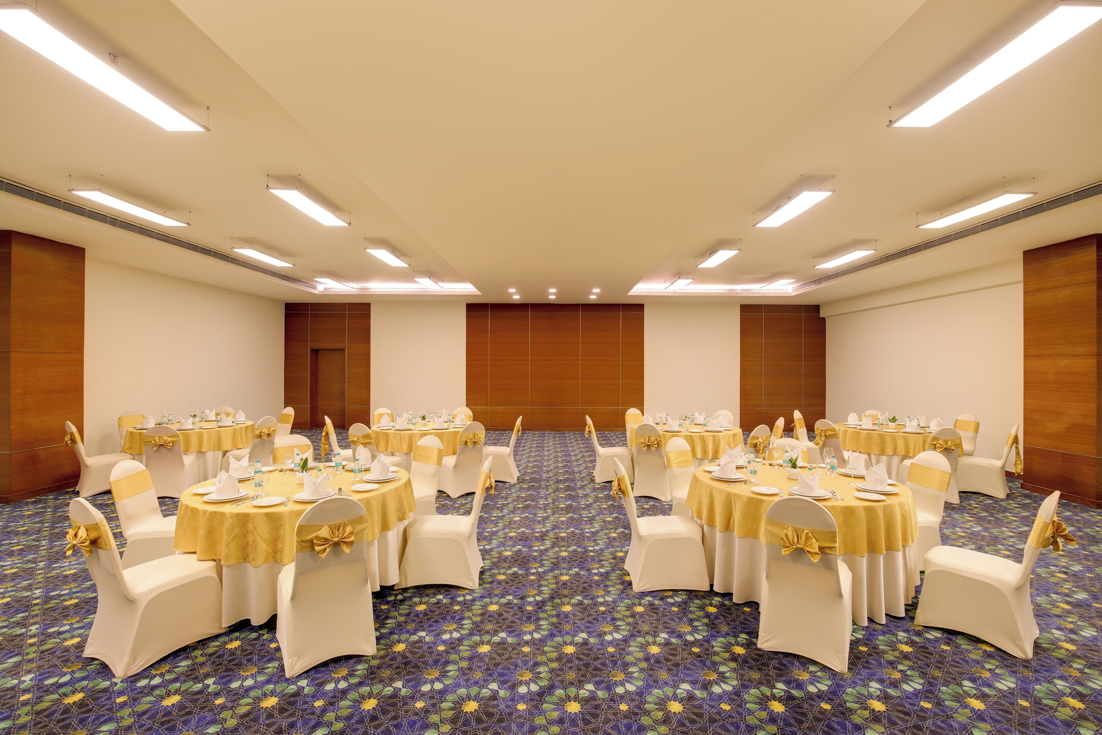 A conference room with round tables, white chairs, and yellow tablecloths.