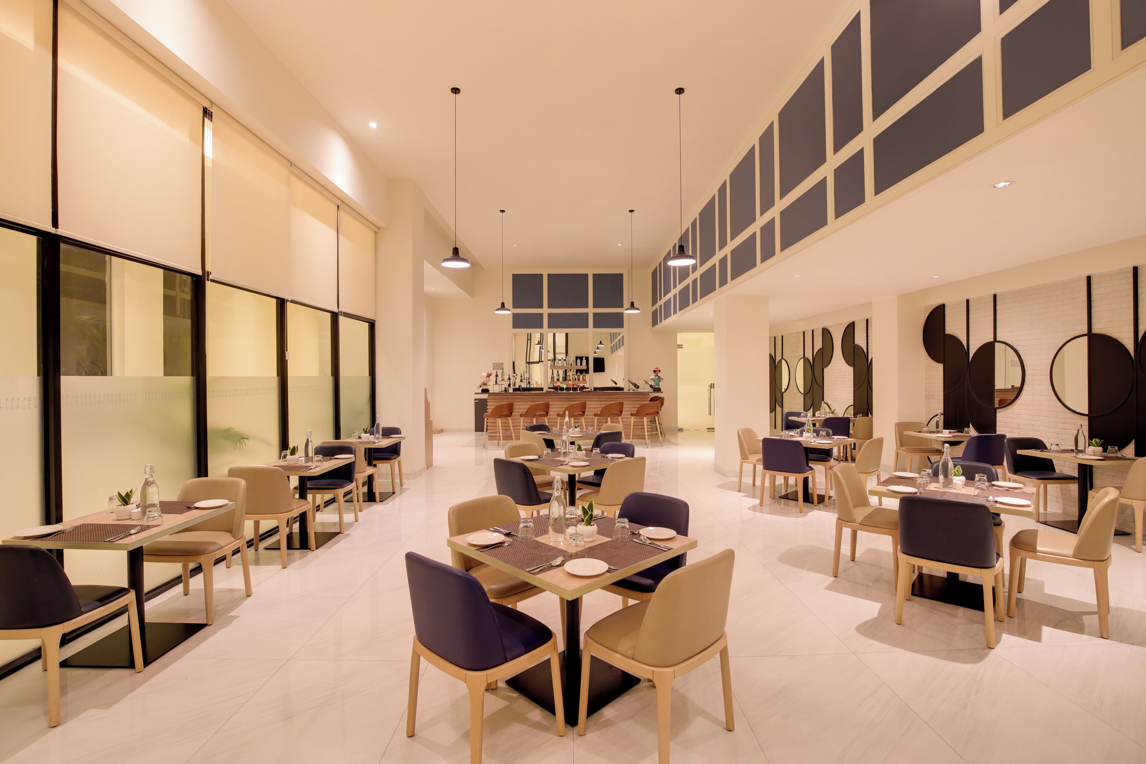 A spacious dining area with multiple tables and chairs, a central bar, and a high ceiling with pendant lighting.