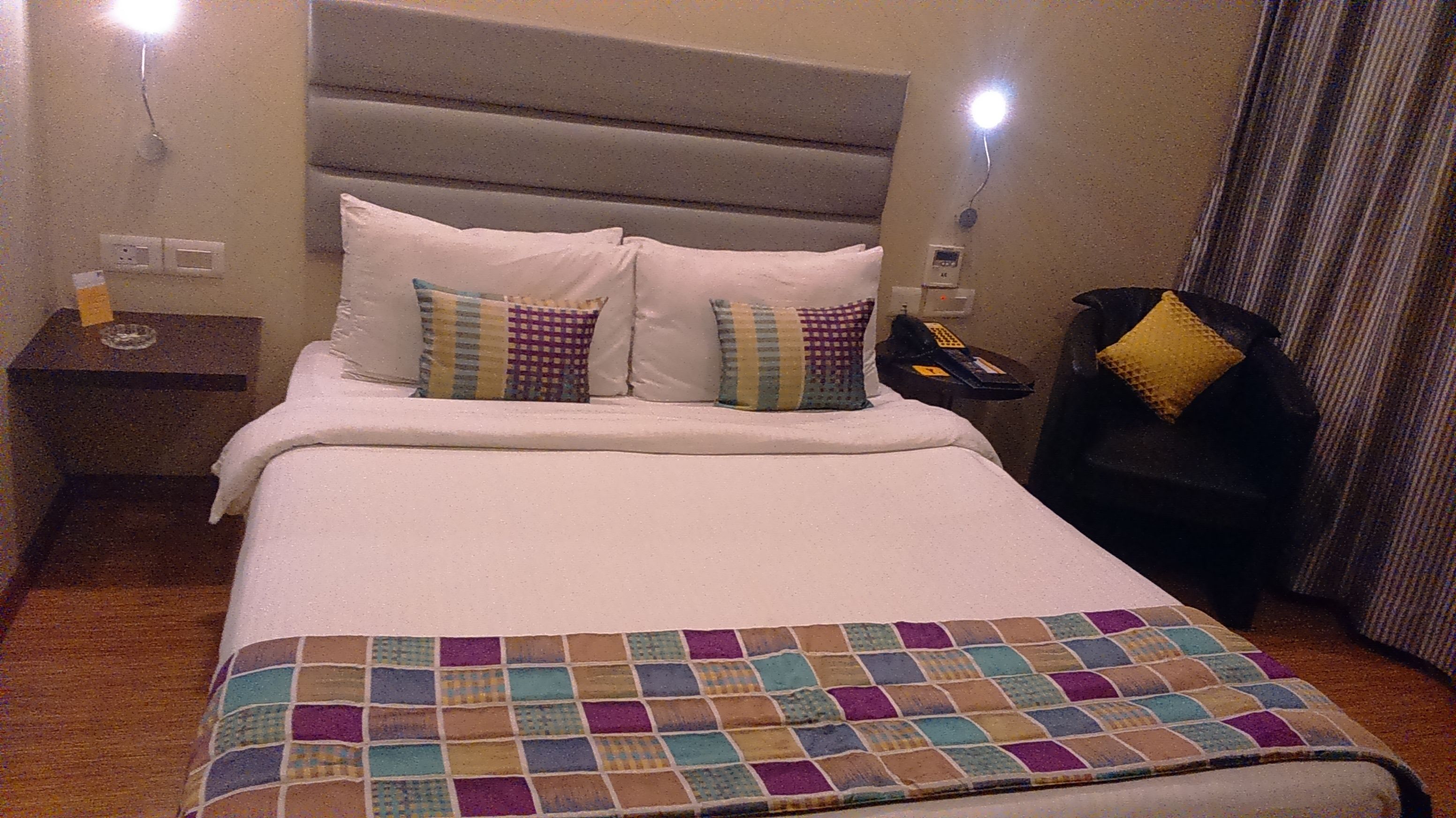 A hotel room with a bed, a nightstand, a telephone, and a lamp.