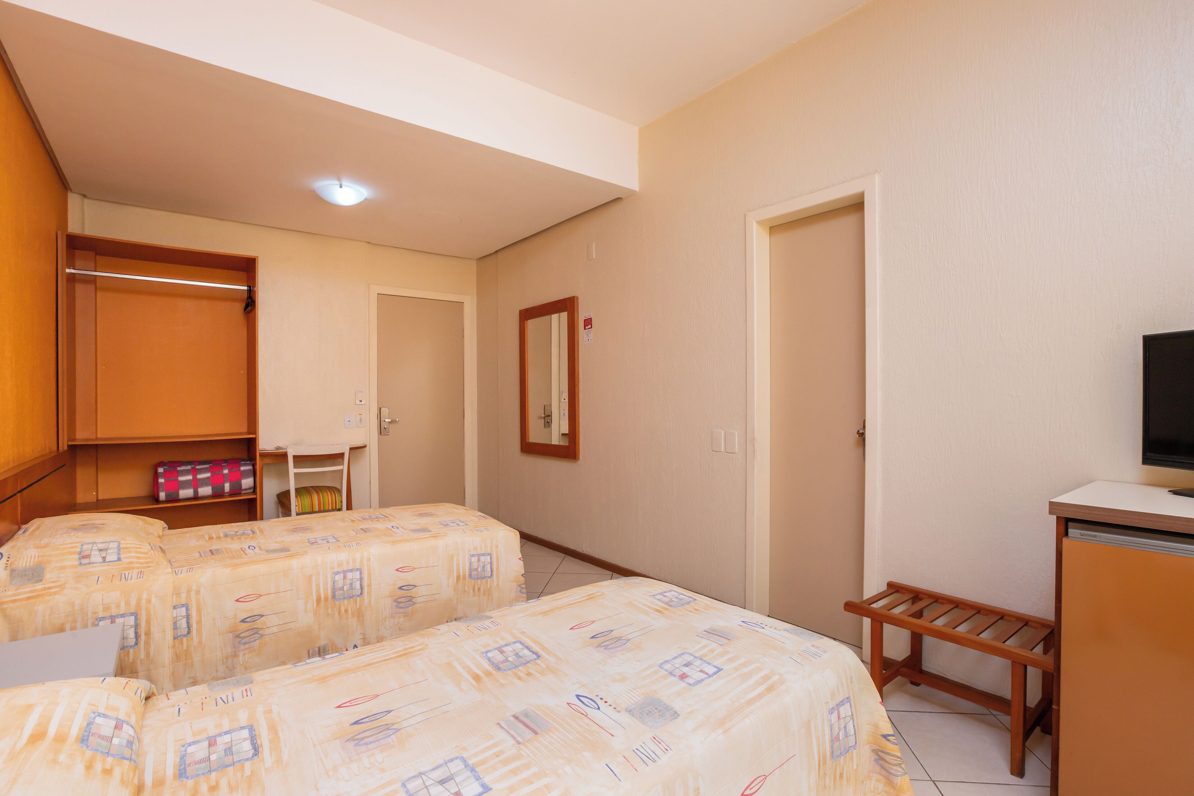 Habitación de hotel con dos camas, un armario, un escritorio y un televisor.