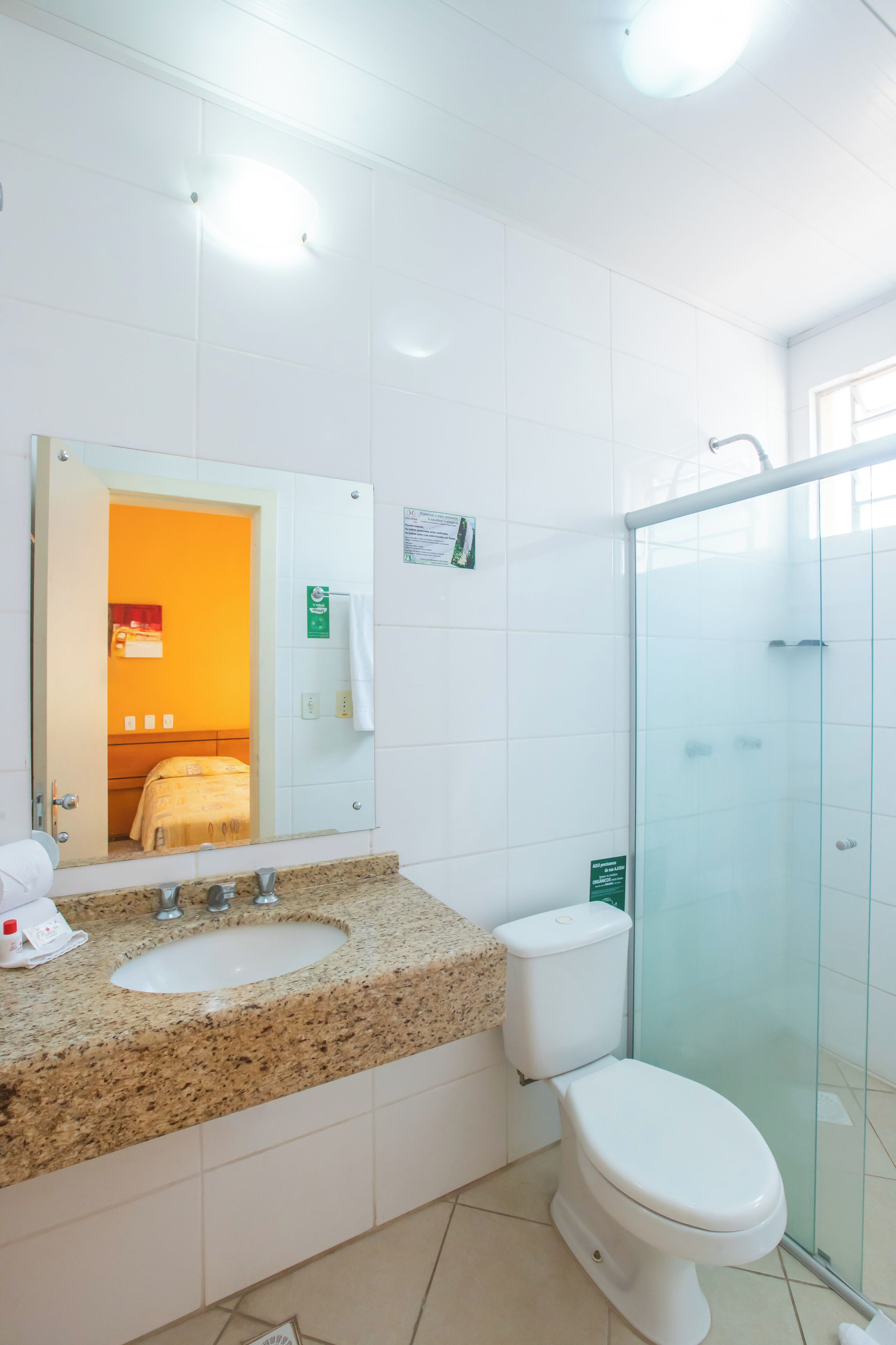 Een hotelbadkamer met een wastafel met een granieten blad, toilet in het wit en een douchecabine van glas.