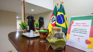 A reception desk with a coffee machine, a jar of matcha powder, a small plant, and two flags. - Confort Hotel (Sao Leopoldo)