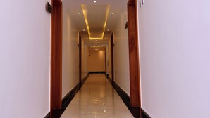 Un couloir d’hôtel avec un sol en marbre poli, un éclairage encastré et des portes en bois.