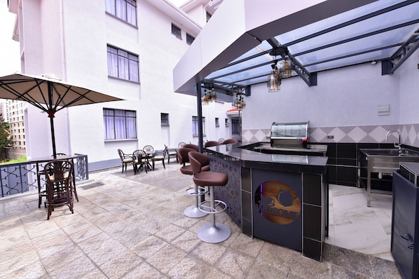 A rooftop bar with a glass enclosure, bar stools, and a seating area with tables and chairs.